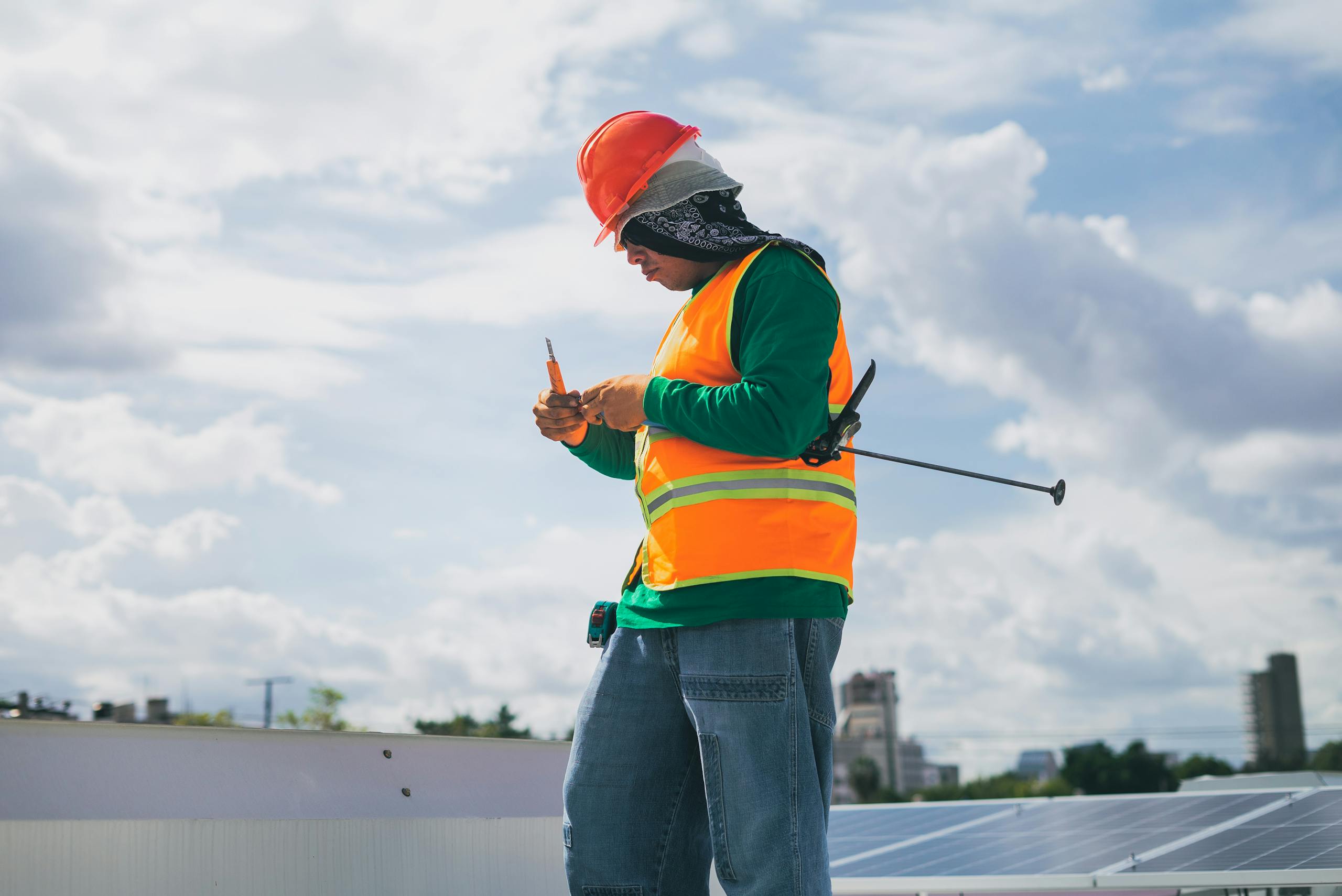 A solar technician in protective gear works on a rooftop under a blue sky.